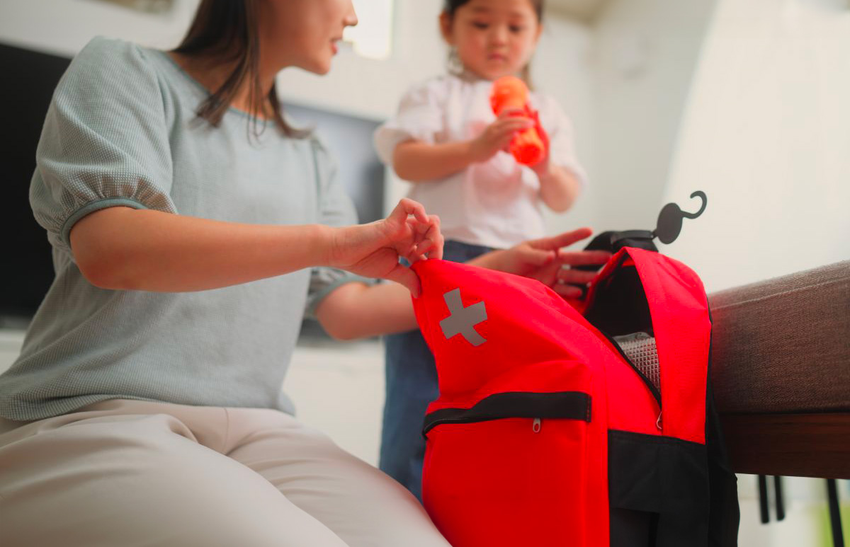 Une mère et sa jeune fille se préparent pour une situation d'urgence. La mère est en train d'ouvrir un sac à dos, tandis que la jeune fille apporte une gourde pour la placer dans le sac.